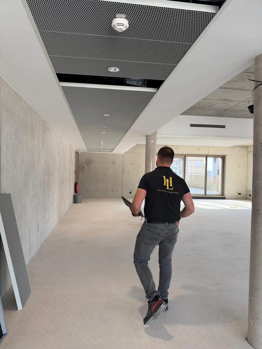 Hariton Lopotenco im HL-Shirt beim Rundgang unter einer Streckmetall-Akustikdecke
